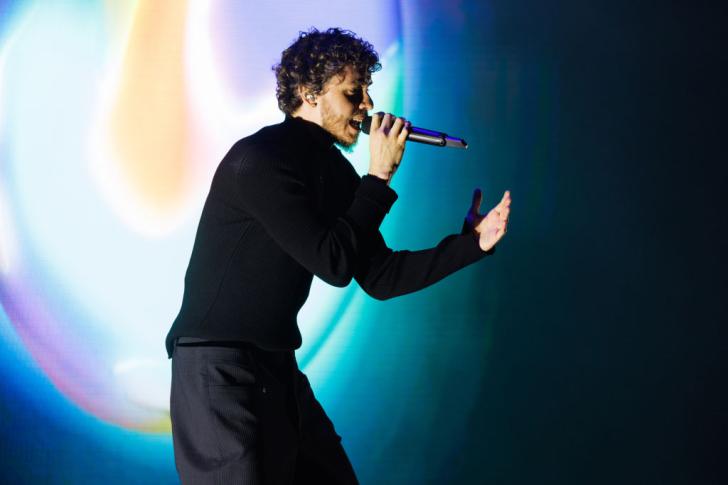 jack harlow gestures on stage while singing into a wireless microphone and wearing all black