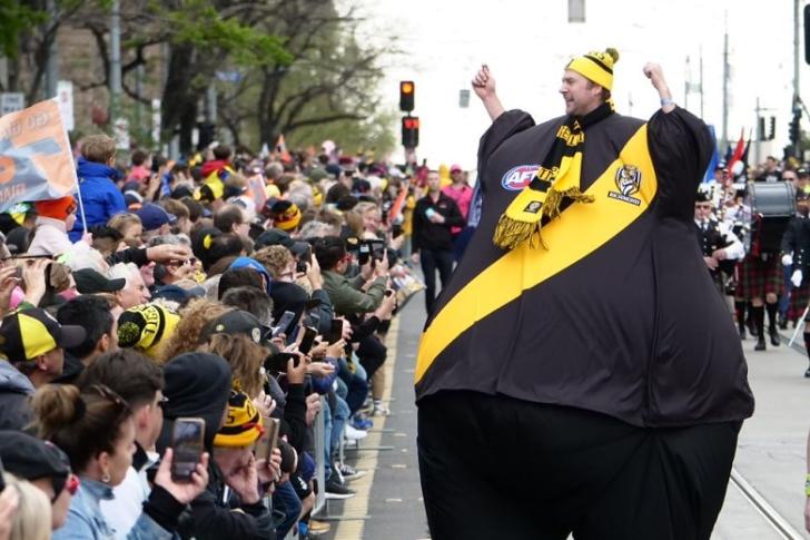 A man in a large Richmond-coloured balloon suit walks down the middle of the grand final parade.