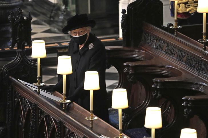 Wearing all black and a face mask, the Queen stands alone in the pews